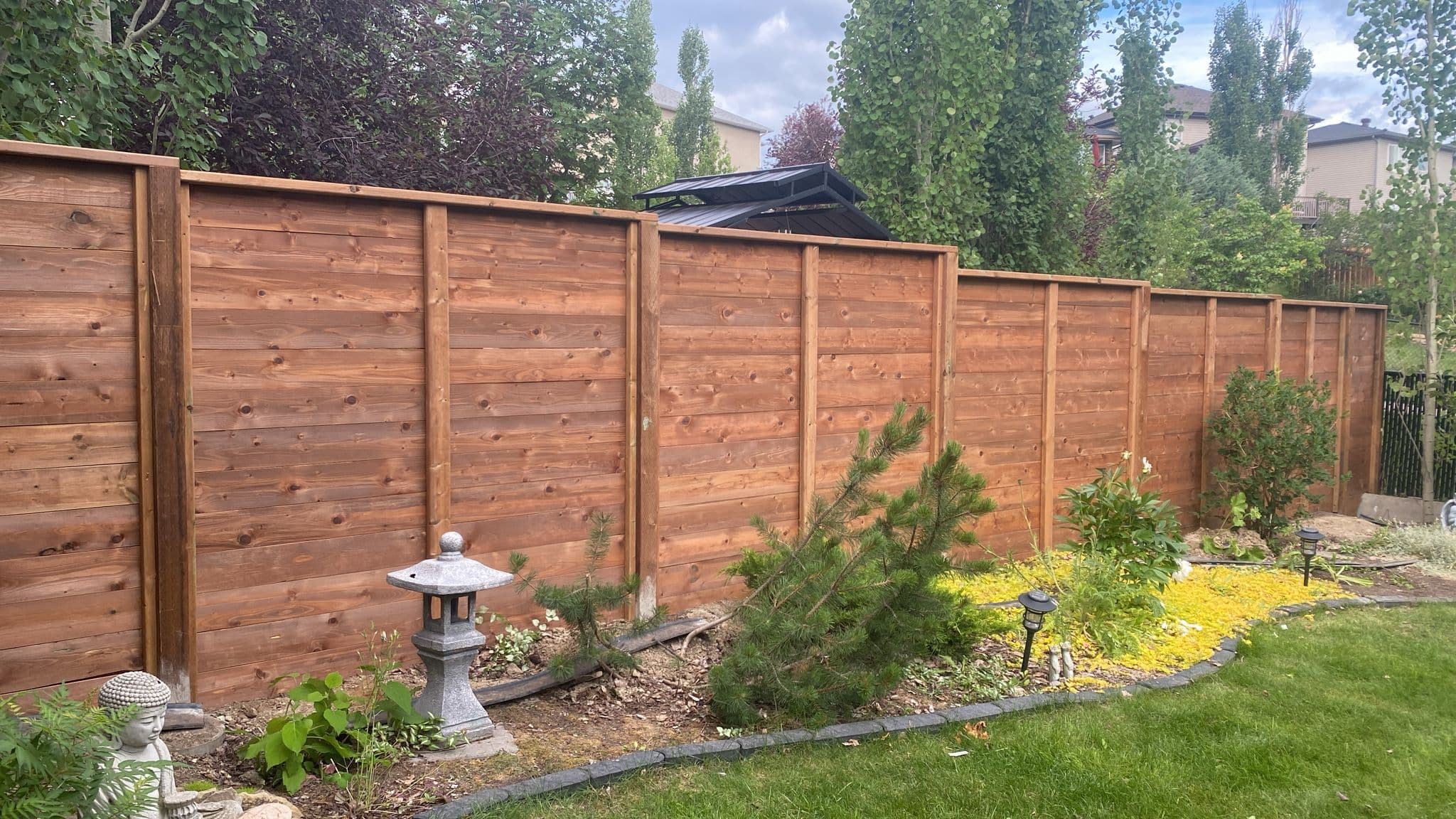 Cedar wood fence installation in Calgary backyard with vertical boards and landscaped yard