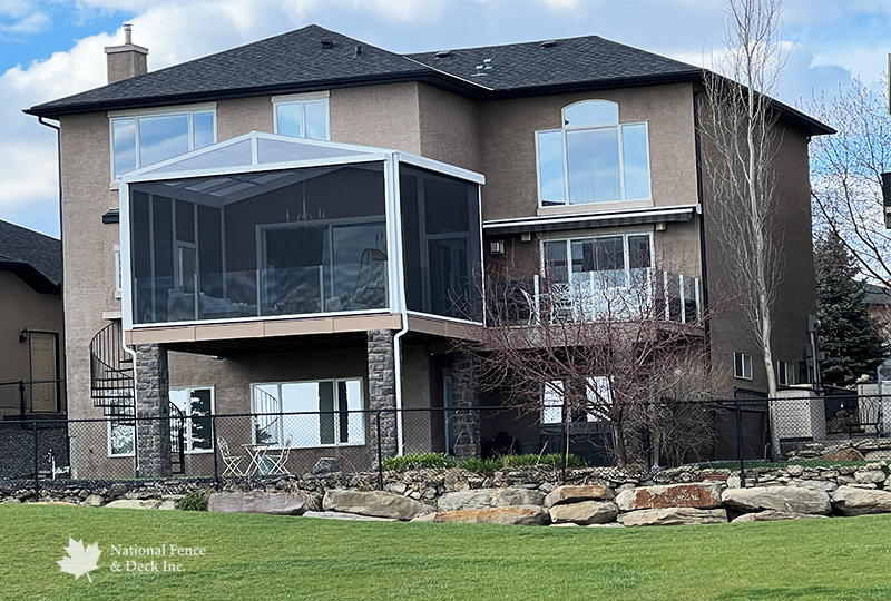 Trex Transcend Lineage Carmel deck with topless glass railings, stone pillars, and a custom roof with a screened room.